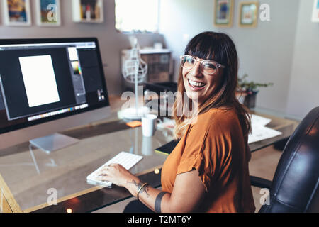 In prossimità di una donna sorridente seduto alla sua scrivania in ufficio con un computer di fronte. Vista laterale di un allegro imprenditrice in ufficio a lavorare sul compute Foto Stock