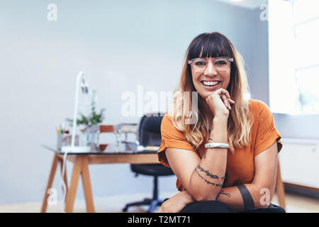 In prossimità di una donna sorridente imprenditore seduto nella sua cabina in corrispondenza di ufficio. Imprenditrice sorridente seduto in ufficio il suo appoggio il mento sulla mano. Foto Stock