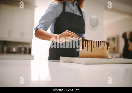 Ritagliato colpo di femmine nel grembiule preparare una torta al cioccolato in cucina. Lo chef donna applicando la glassa di torta. Foto Stock