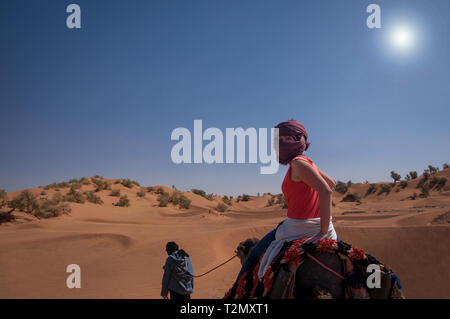 Giovane donna felice a cavallo su dromedario nel deserto del Sahara - Marocco Foto Stock