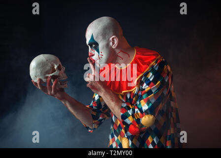 Ritratto di mad sanguinosa clown mostra tranquillo segno al cranio, faccia nel sangue. L'uomo con il trucco in costume di halloween, maniac Foto Stock