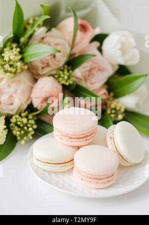 Elegante dolce macarons e color pastello beige fiori sul tavolo bianco closeup Foto Stock