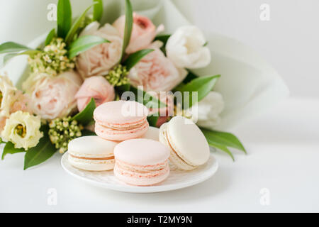 Elegante dolce macarons e color pastello beige fiori sul tavolo bianco closeup Foto Stock