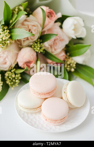 Elegante dolce macarons e color pastello beige fiori sul tavolo bianco closeup Foto Stock