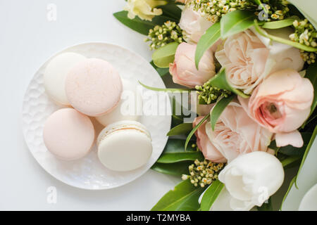 Elegante dolce macarons e color pastello beige fiori sul tavolo bianco closeup Foto Stock