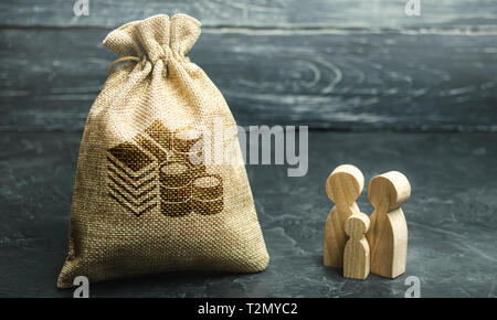 Miniatura in legno figurine famiglia stare vicino a un sacco di denaro. Il concetto di risparmio. Pianificazione del bilancio. Distribuzione degli utili. Gestione finanziaria. Accu Foto Stock