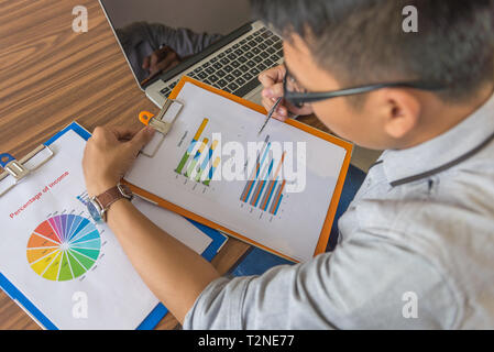 Giovane uomo che tiene la penna che punta al grafico nel documento Foto Stock