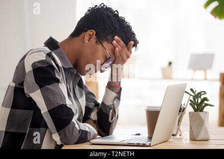 Vista laterale ha sottolineato africani stanchi business donna seduta che soffrono di mal di testa si sente male toccare fronte con gli occhi chiusi. Frustrati femmina nero Foto Stock