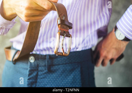 Giovane uomo in una Camicia a Righe mette su un nastro in pantaloni vicino. Mettere sul concetto di vestiti Foto Stock