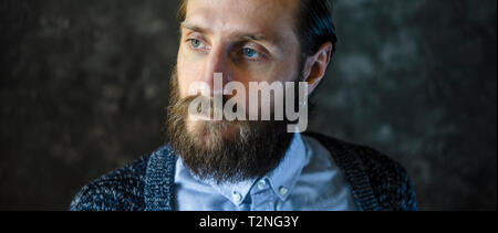 Ritratto di moda di un pensieroso uomo barbuto in una camicia blu e blu cardigan lavorato a maglia su sfondo grigio. Riflessività Concept Foto Stock