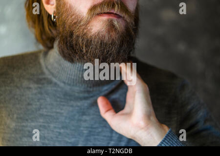 Barbuto Giovane Turtleneck maglione grigio tiene per mano dalla gola. Sintomo del concetto di malattia Foto Stock