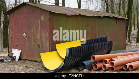 Nuove plastiche tubi fognari e grondaie si trovano nei pressi di un metallo arrugginito capannone rustico. Giornata di Primavera paesaggio rurale Foto Stock