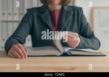 Imprenditrice libro di lettura alla scrivania in ufficio, cercando il business informazioni correlate Foto Stock