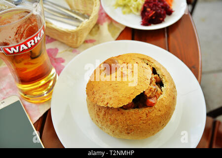 Cucina tradizionale con il polacco spezzatino di maiale in pane e più antico di Warka bier nel bistro della città vecchia a Krakowskie Przedmiescie street a Varsavia, Polonia Foto Stock