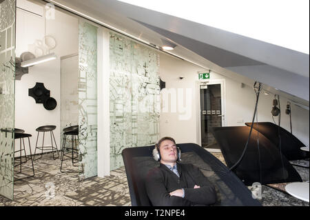 Un giovane uomo bianco si rilassa ascoltando musica in un ambiente aziendale. Foto Stock