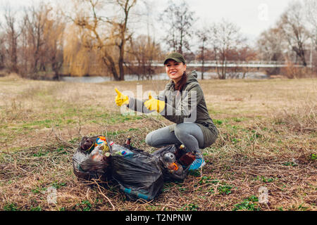 Donna volontario ripulito il cestino nel parco. Persone prelevati spazzatura e mostra il risultato con sacchi pieni e pollice in alto. Ecologia e ambiente concep Foto Stock