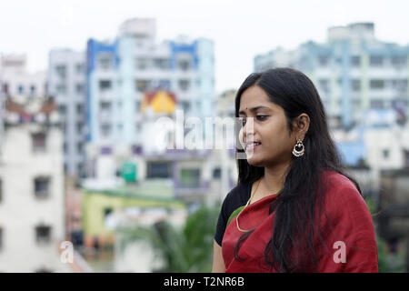 Bellissimo Indian Bengali la signora in rosso sari in piedi sul tetto con paesaggio urbano sfondo Foto Stock