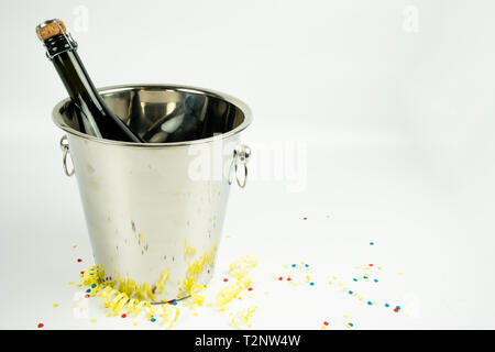 Una bottiglia di champagne in un secchio di metallo su uno sfondo bianco. con i confetti intorno al cucchiaio. Vogliamo festeggiare con una bottiglia di champagne Foto Stock