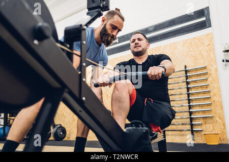 Personal trainer lavora con uomo con disabilità sulla macchina a remi Foto Stock