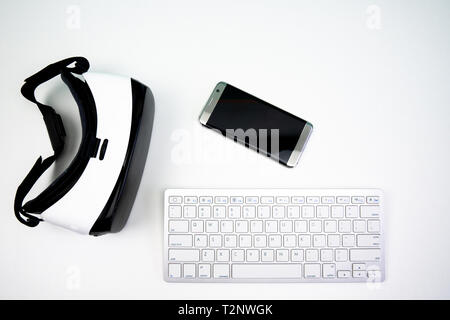 Vista dall'alto di differenti tecnologie wireless su uno sfondo bianco. Una realtà virtuale auricolare, controller di gioco, tastiera e uno smartphone Foto Stock