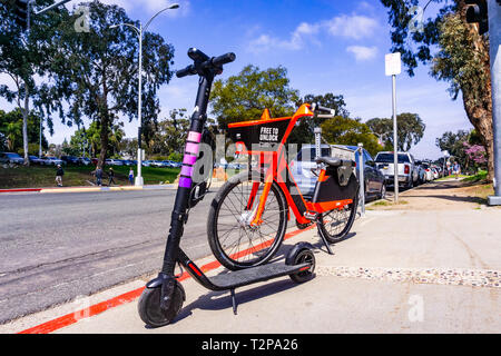 Marzo 19, 2019 San Diego / CA / STATI UNITI D'AMERICA - Salto bicicletta elettrica (di proprietà di Uber) e Lyft Escooter parcheggiato a fianco a fianco sul marciapiede, vicino parcheggiata vicino Balbo Foto Stock