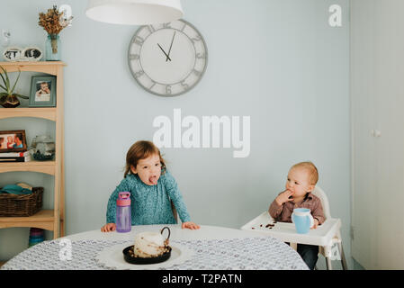 Toddler femmina a tavola e baby fratello in sedia alta Foto Stock