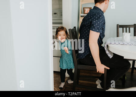 Toddler femmina nascondendo dal padre a tavola Foto Stock