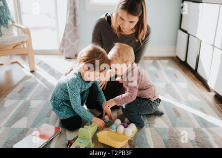 Toddler femmina giocando con la madre e il bambino fratello in salotto Foto Stock