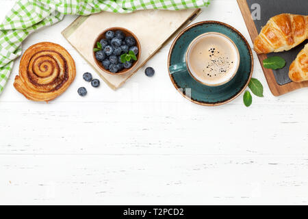 Caffè, cornetti, panini alla cannella e le bacche di prima colazione. Su un tavolo di legno. Vista da sopra con copia spazio per il testo Foto Stock