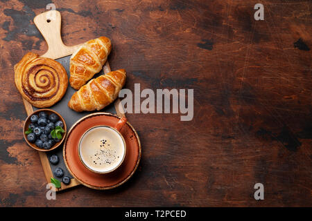Caffè, cornetti, panini alla cannella e le bacche di prima colazione. Su un tavolo di legno. Con il blocco note per il testo Foto Stock
