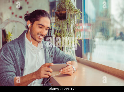 Barbuto uomo felice guardando phone sorridente. Closeup ritratto di un bel ragazzo indossa formale maglietta bianco, grigio camicetta seduta vicino alla finestra nella tavola Foto Stock