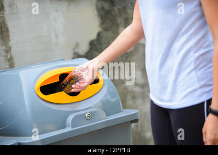Stretta di mano la donna a buttare via la bottiglia di plastica nel contenitore di riciclaggio Foto Stock