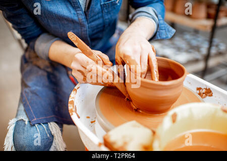 Donna fare brocca di argilla formando una forma con un attrezzo speciale sulla ruota di ceramiche, vista da vicino Foto Stock