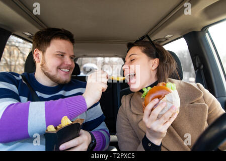 Coppia giovane di mangiare fast food in auto. moderno stile di vita del ritmo Foto Stock