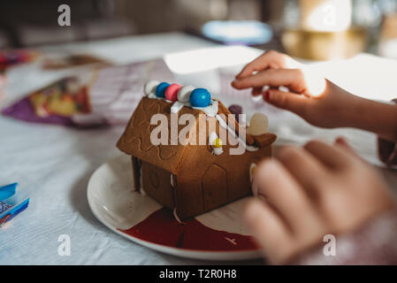 Bambino con le mani in mano la decorazione di una casa di panpepato Foto Stock