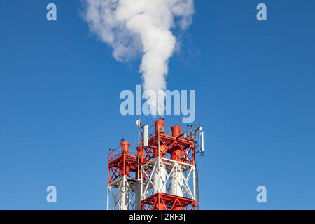White nocivi del fumo proveniente al di fuori del rosso-e-bianco con tubi di comunicazione mobile antenne in una fabbrica nel centro della città contro lo sfondo di Foto Stock