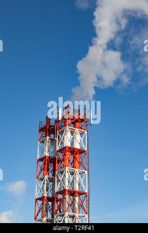 White nocivi del fumo proveniente al di fuori del rosso-e-bianco con tubi di comunicazione mobile antenne in una fabbrica nel centro della città contro lo sfondo di Foto Stock