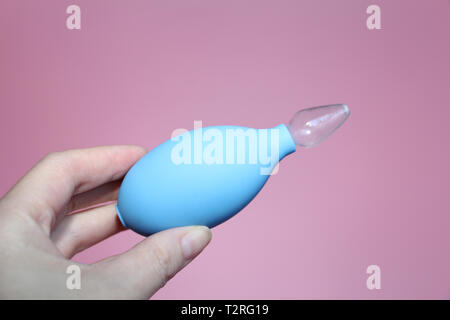 Blu Aspiratore nasale con punta di vetro in mano femminile. Aspirazione di scarico dal tubo di lancio del bambino. Sfondo rosa. Foto Stock