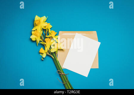 Bouquet di fiori daffodil con una busta biglietto di auguri su uno sfondo blu Foto Stock
