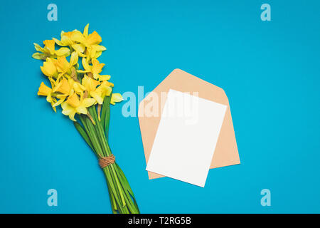 Freschi bouquet di fiori di narciso e la busta con la lettera su uno sfondo blu. minimalismo Foto Stock