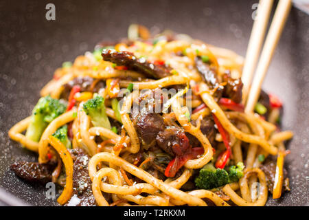 Udon Stir-Fry Tagliatelle con manzo e verdure in padella Wok su sfondo scuro Foto Stock