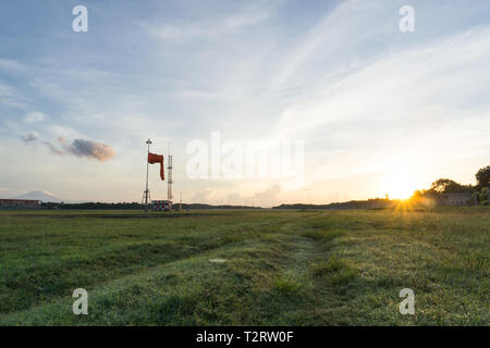 Sunrise all'aeroporto di Bali. Mattina vibes dal luminoso cielo chiaro. Aspetto di erba verde e guardare il calzino di vento, il vento è calmo Foto Stock