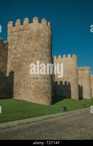 Fiancheggiata torri di pietra sulla grande parete della città in stile romanico accanto alla strada di Avila. Con un imponente muro intorno al quartiere Gotico della città in Spagna. Foto Stock