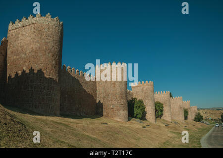 Fiancheggiata torri di pietra sulla grande parete della città in stile romanico accanto alla strada di Avila. Con un imponente muro intorno al quartiere Gotico della città in Spagna. Foto Stock