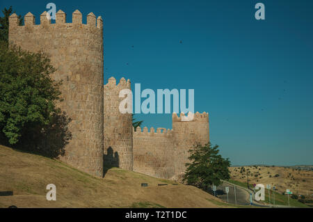 Fiancheggiata torri di pietra sulla grande parete della città in stile romanico accanto alla strada di Avila. Con un imponente muro intorno al quartiere Gotico della città in Spagna. Foto Stock
