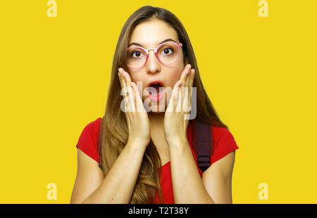 Studente sorpreso con gli occhiali su sfondo giallo Foto Stock