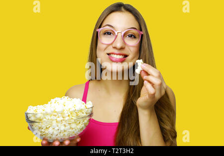 Felice Allegra donna mangiare pop corn guardando al lato su sfondo giallo. Ragazza con grande ciotola di vetro con cinema porzione di pop corn. Foto Stock