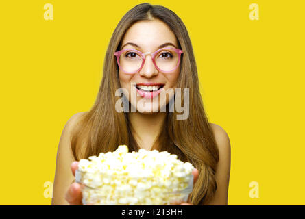 Felice allegro attraente giovane donna nerd tenendo i pop corn isolato della benna su sfondo giallo Foto Stock