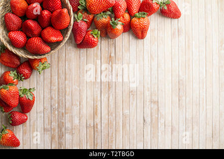 Fragole spazio copia con un piccolo cestino di fragole nell'angolo superiore sinistro circondato da fragole sparsi su un sfondo di legno preso Foto Stock