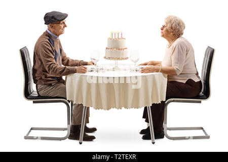 Anziano uomo e donna celebrando con una torta di compleanno a un tavolo isolato su sfondo bianco Foto Stock